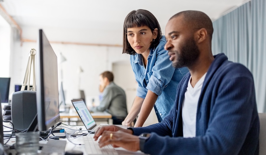 Two businesspeople looking at desktop computer monitor and discussing work at desk