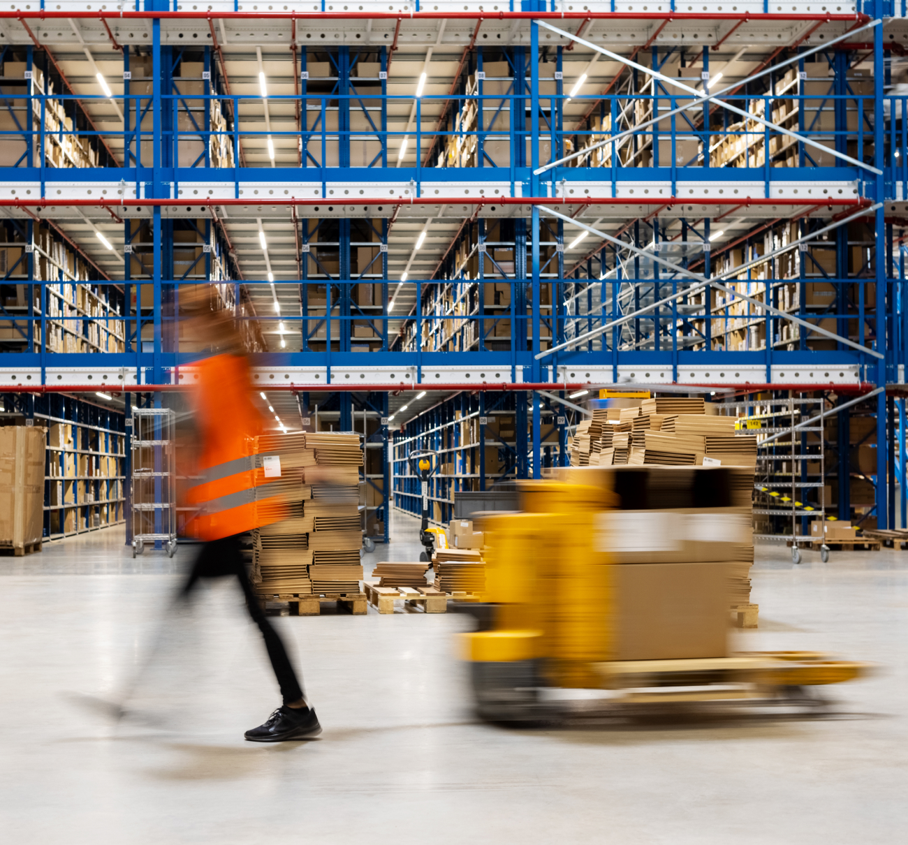 Factory worker in blaze orange vest walking past a pallet